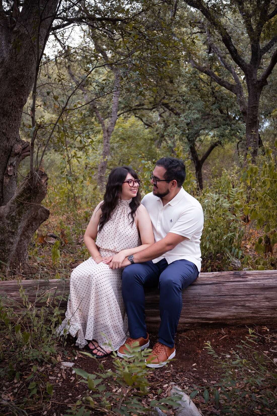 Carolina y Brian sentados en un tronco, mirándose sonrientes