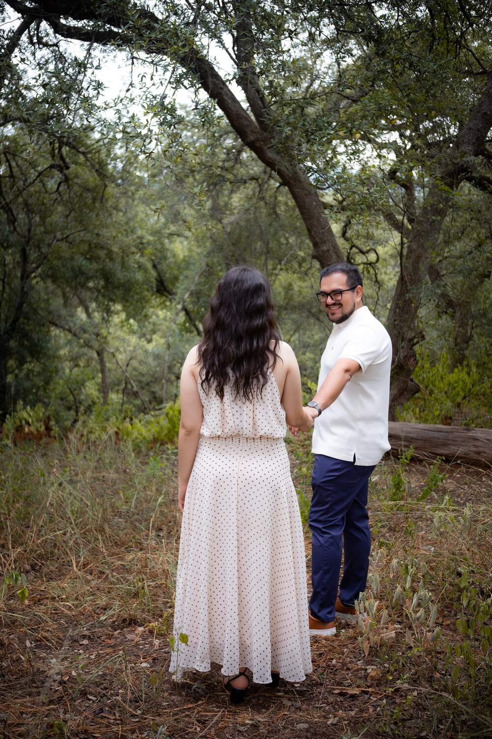 Brian sonríe mientras toma de la mano a Carolina en el bosque